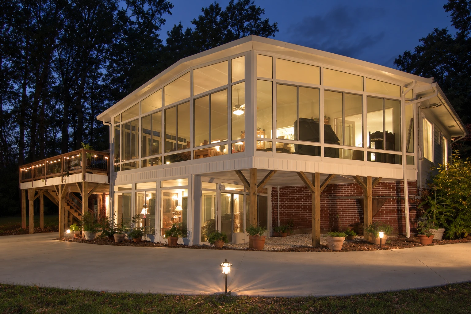 Custom sunroom with large illuminated windows on an elevated home, shown at night.
