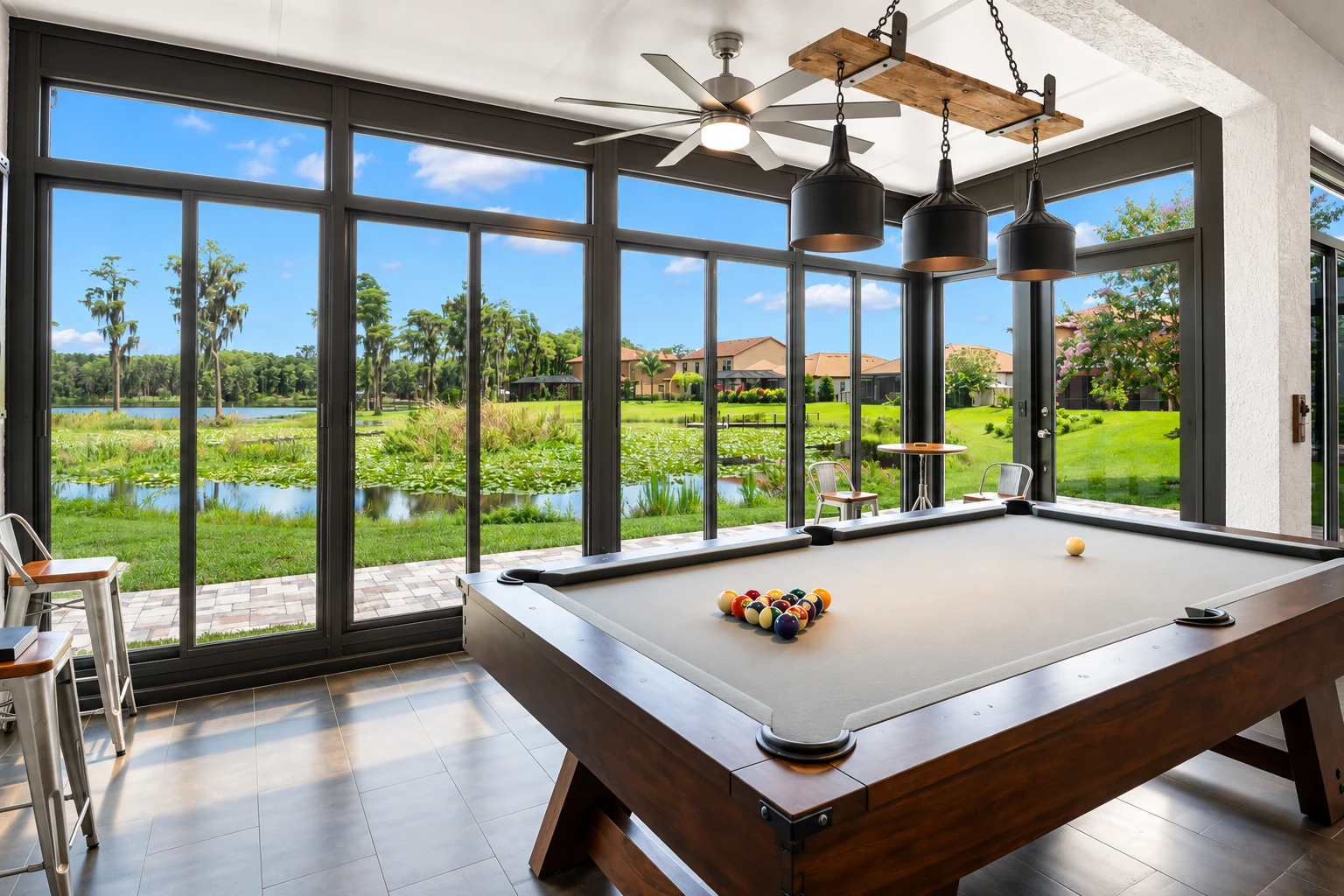 Enclosed patio with dark-framed windows, a pool table and views of a green lakeside yard.
