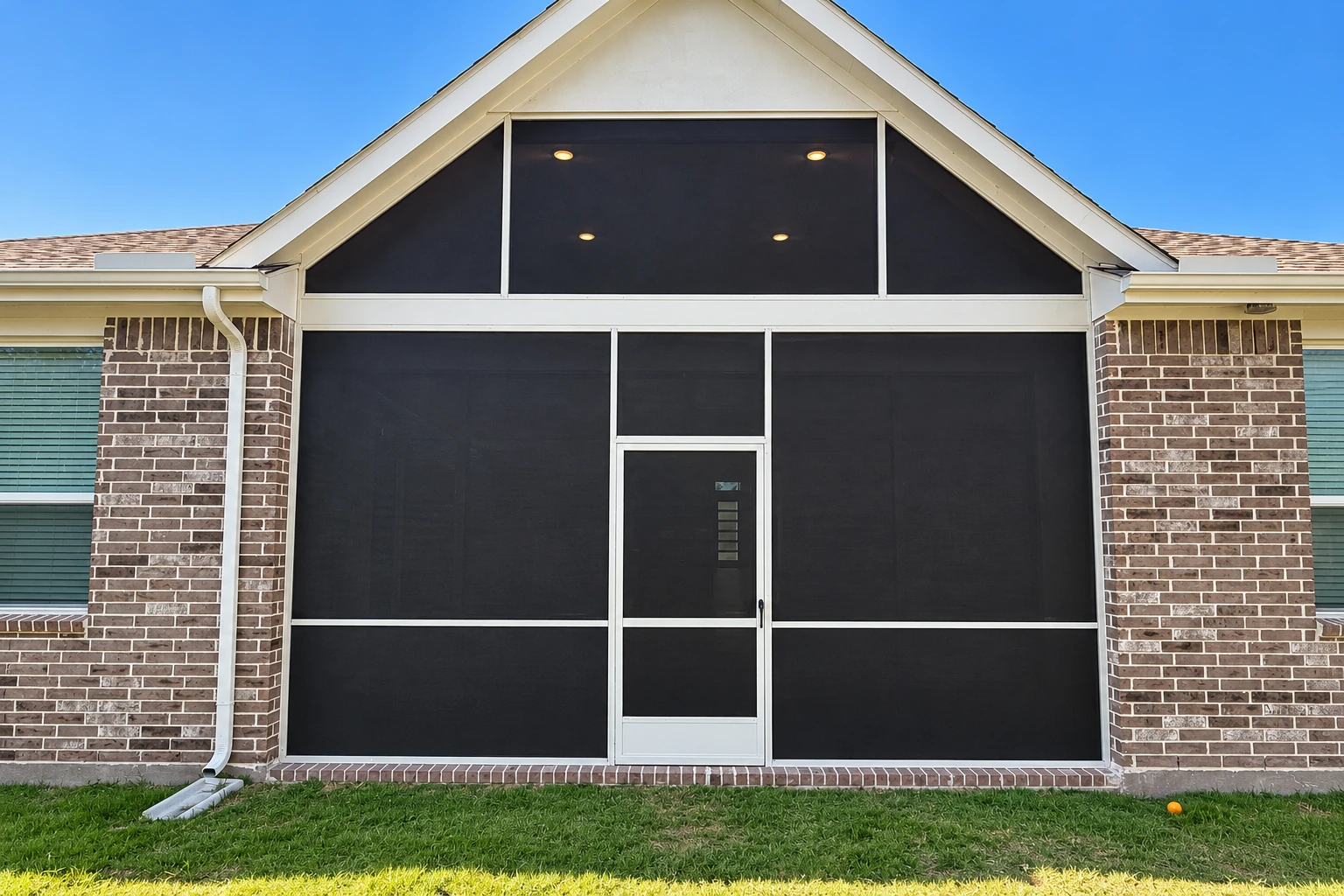 Screen room installation with dark mesh panels, white framing, and a centered entry door on a brick house.